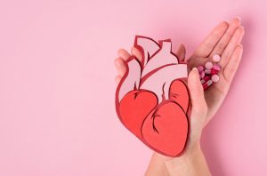 Woman's hands holding a paper cut-out of a human heart in one hand and pills in another