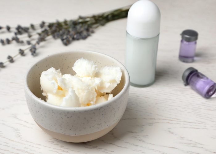 A bowl of thick white mixture for natural deodorant, a stick of deodorant, vials of lavender essential oils and sprigs of dried lavender in the background
