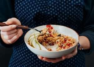 Woman holding a bowl of. homemade yogurt with oats, nuts, and fruits