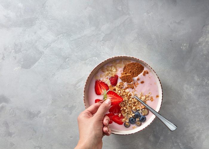 Woman putting a strawberry topping in her bowl of homemade strawberry yogurt with oats, nuts and berry toppings