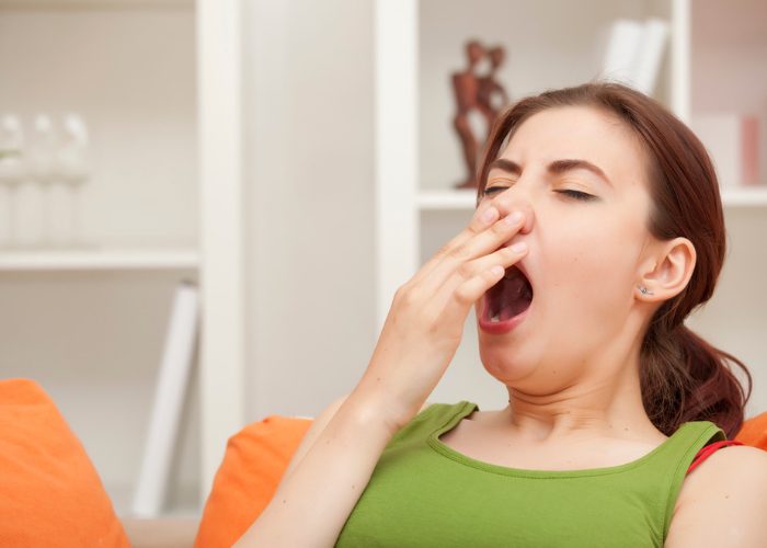 Woman yawning widely on the couch in her living room