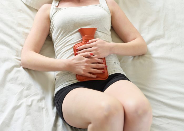 Woman in bed holding a hot water bottle to her abdomen to relieve painful menstrual cramps