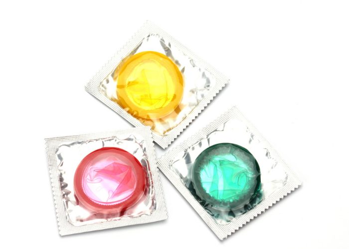 Three packets of colored condoms in yellow, red, and green