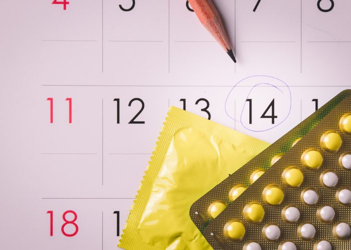 A calendar with a circled date, a condom packet, and two packs of contraceptive pills