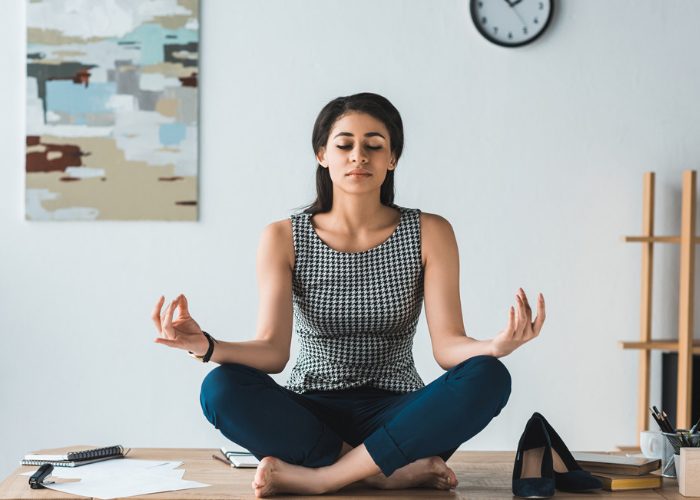 Woman sitting on her work desk with heels off practicing meditation