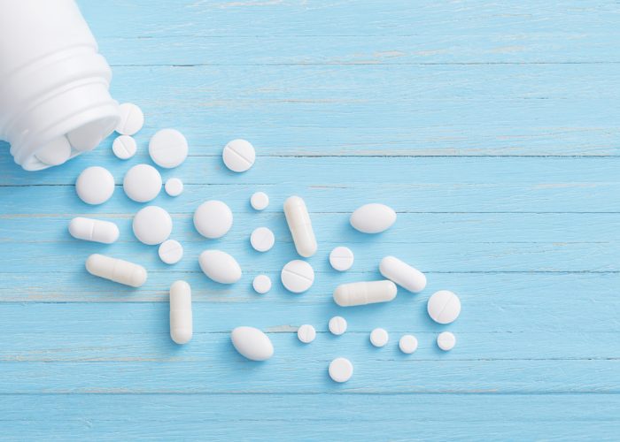 An unlabeled medicine bottle spilling out white tablets and capsules of different shapes and sizes on a blue wooden table.