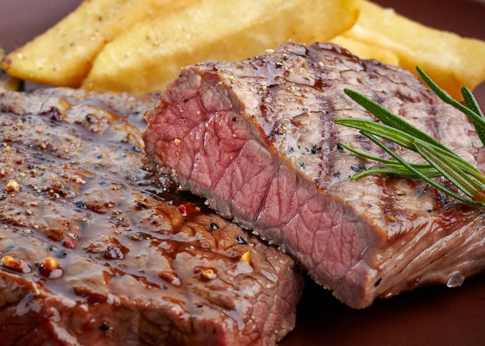 A closeup of juicy medium-rare pepper steak rich in vitamin B12 with a side of French fries