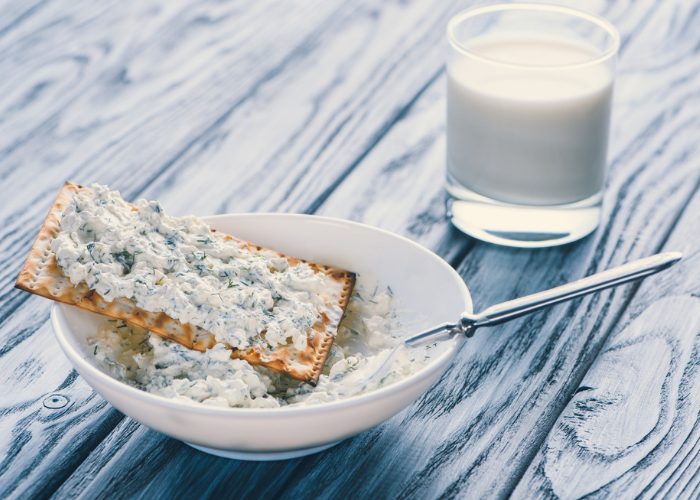 A bowl of blue cheese spread with a cracker on top, with a glass of milk in the background.