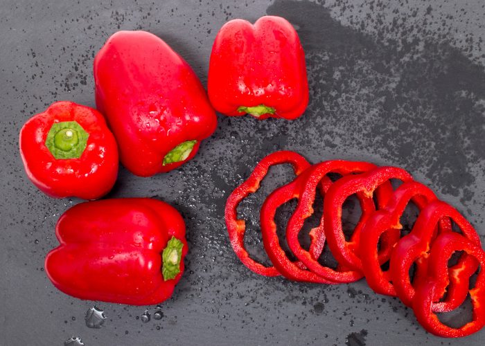 Whole and sliced red peppers that are rich in the amino acid leucine, laid out on a grey table 