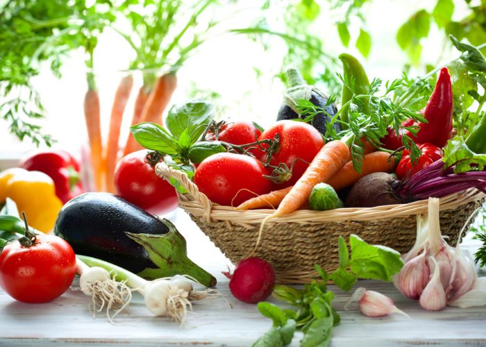 Vegetables such as tomatoes, carrots, eggplant, garlic, and spring onions rich in the amino acid methionine, in a wooden basket and also on a table 