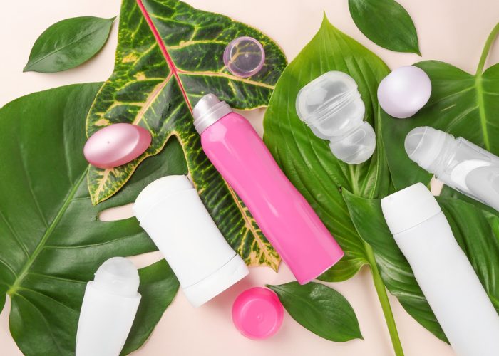 Antiperspirant bottles and. deodorant sticks on large green leaves on a wooden table