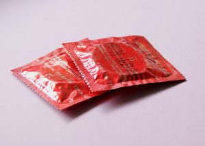 Two unopened red condom packets on a pink table