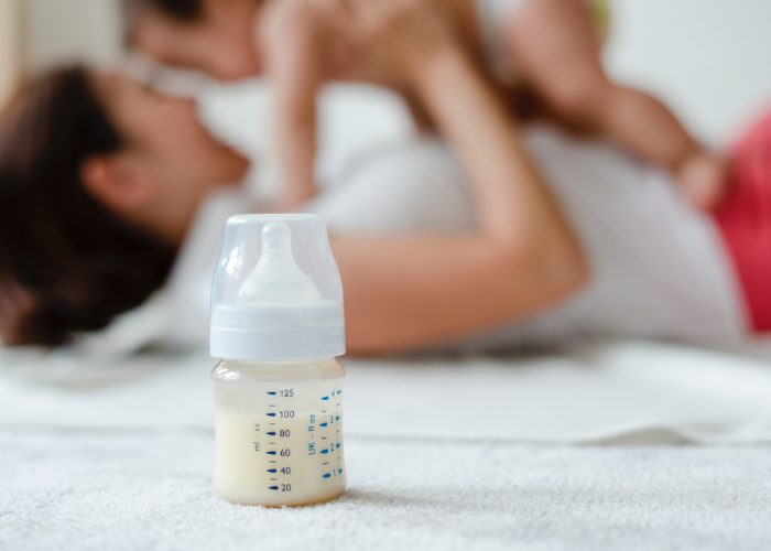 Focus on a milk bottle with a mother holding her baby in the background
