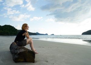 Childfree woman sitting on a log on the beach looking out on the horizon