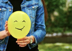 Nulliparous woman in denim jacket holding onto a yellow balloon with a smiley face drawn on it