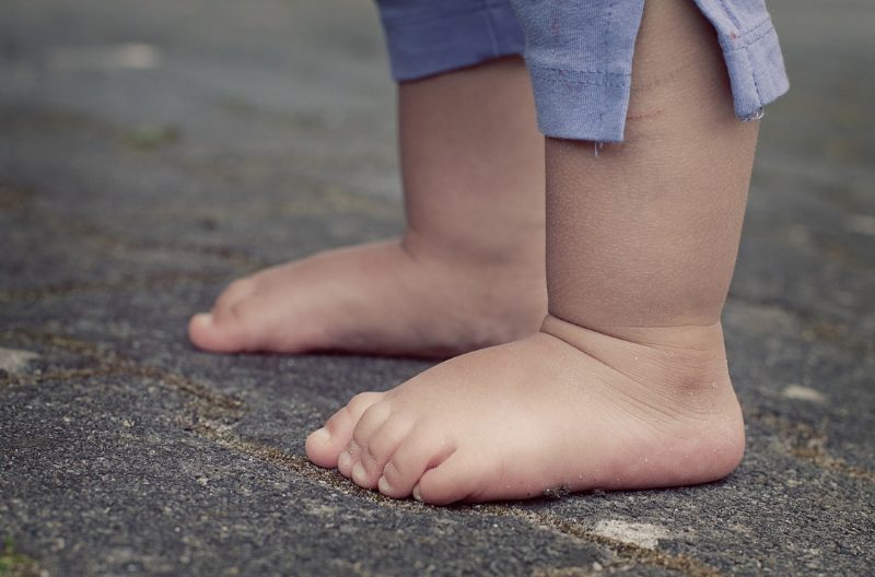 Closeup of feet of a young toddler in blue shorts barefoot on the ground
