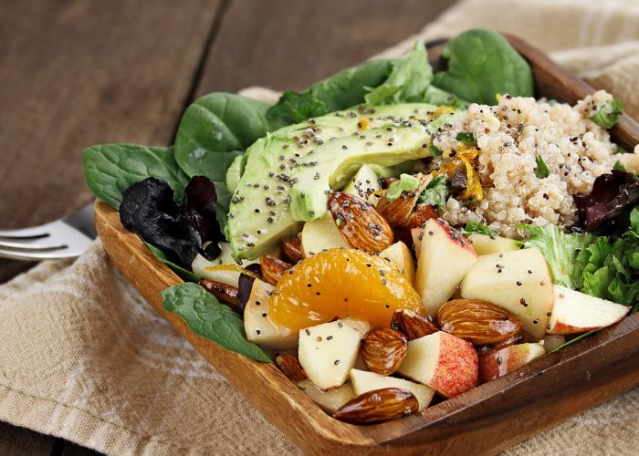 A plant-based dish of spinach, avocado, nuts, and sliced fruit on a wooden plate
