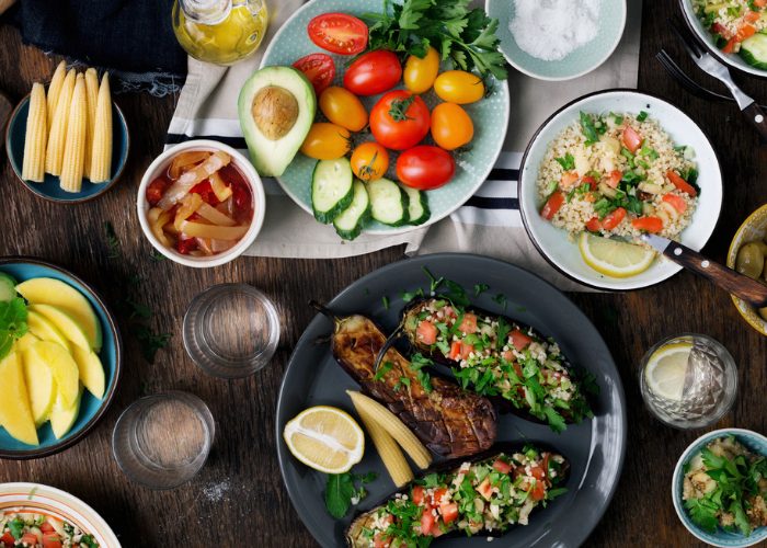 A table filled with different plant-base dishes such as grilled eggplant, fresh tomatoes, avocado, and quinoa