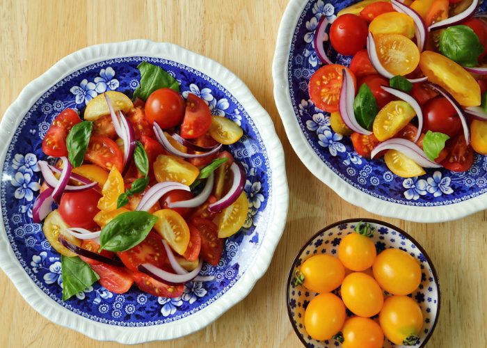 Two plates of mixed red and yellow tomato salads with sliced onion and basil