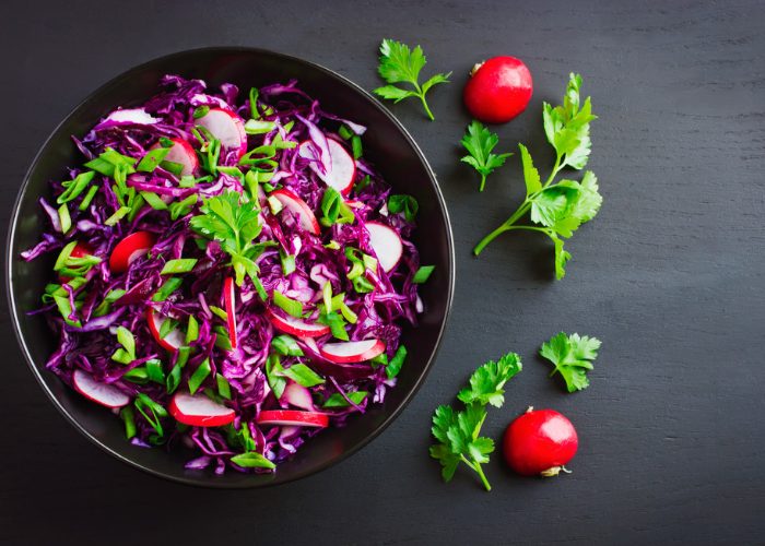A bowl of purple cabbage, sliced small red radishes, and green parsley leaves in a black bowl on a black table