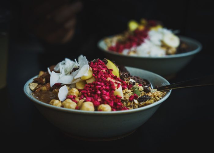 Healthy breakfast bowls of oats, nuts, seeds, dried fruit, coconut shavings, and vegan chocolate yogurt