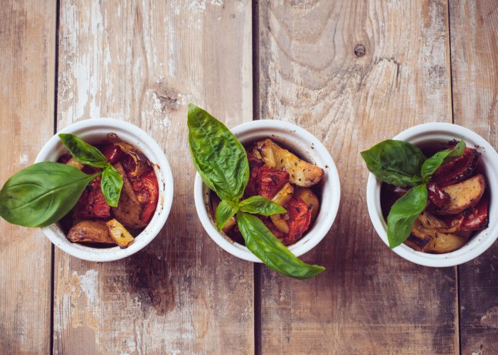 Three small ramekin bowls filled with grilled vegetables topped with fresh basil sprigs