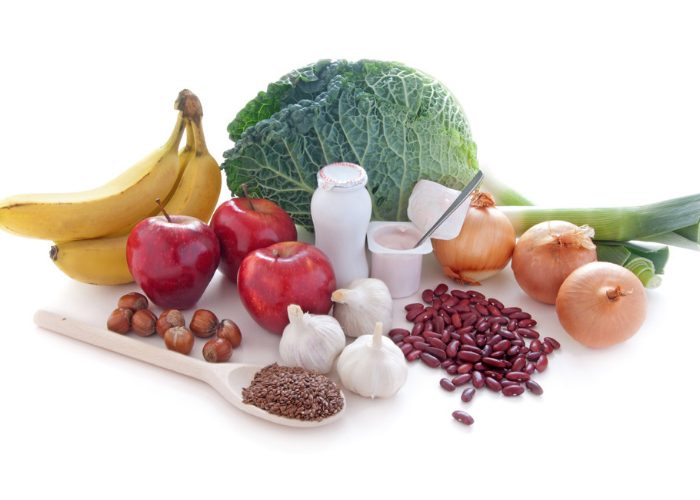 different prebiotic and probiotic foods such as bananas, apples, kidney beans, yogurt, onions, garlic etc. on a white surface