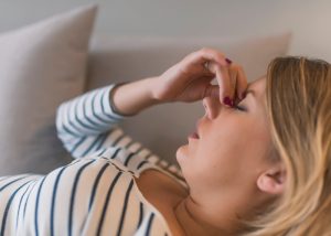 Woman with a migraine lying on her couch holding her forehead in pain