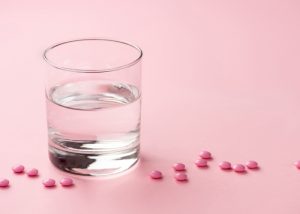 A glass of water and pink pills scattered on a pink table