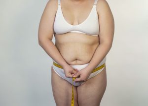 Obese woman in just wearing white underwear measuring her waist with a measuring tape