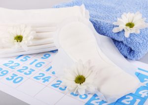 Sanitary pads, blue towels, and white flowers on top of a calendar