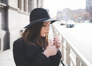 A young woman in a black hat and black coat lighting a cigarette