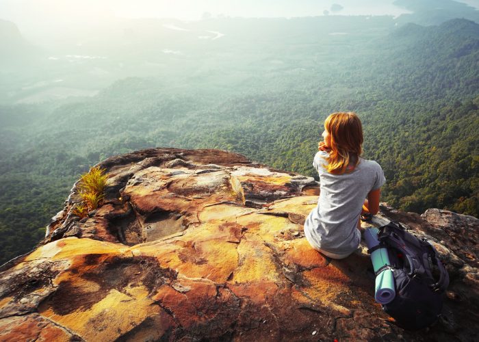 Solo woman backpacker sitting on top of a cliff looking down at the forests below