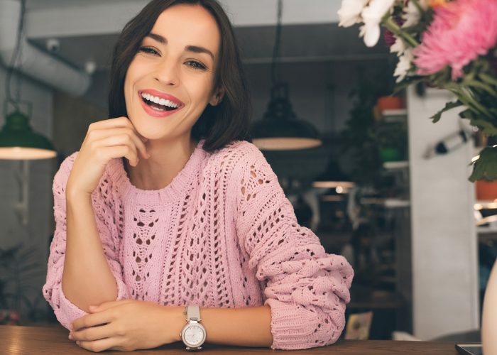 Woman in pink knitted sweater sitting at a cafe smiling