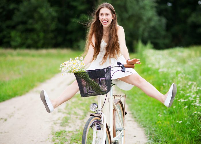 Young woman with a big smile riding a bicycle with her legs up in the air