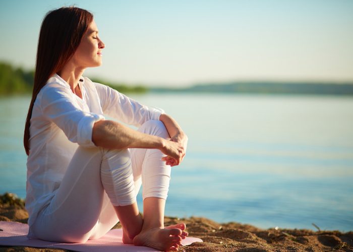 Peaceful and content woman sitting by a lake with her eyes closed and smiling