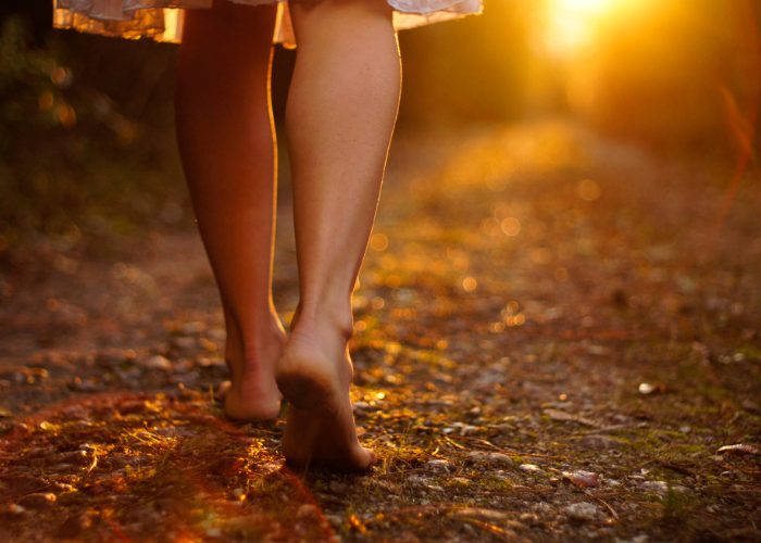 Close up of woman's bare feet walking on dirt road in the forest at sunset