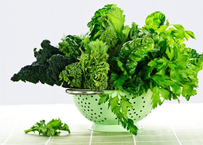 Leafy greens rich in the amino acid tryptophan, sitting in a green colander on a green table
