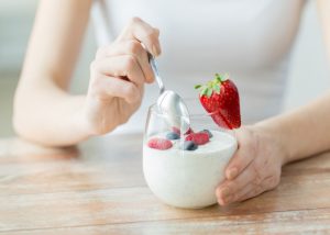 Woman eating yogurt topped with berries in a clear glass