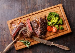 Vitamin B12-rich steak on a wooden board with broccoli and cherry tomatoes on the side