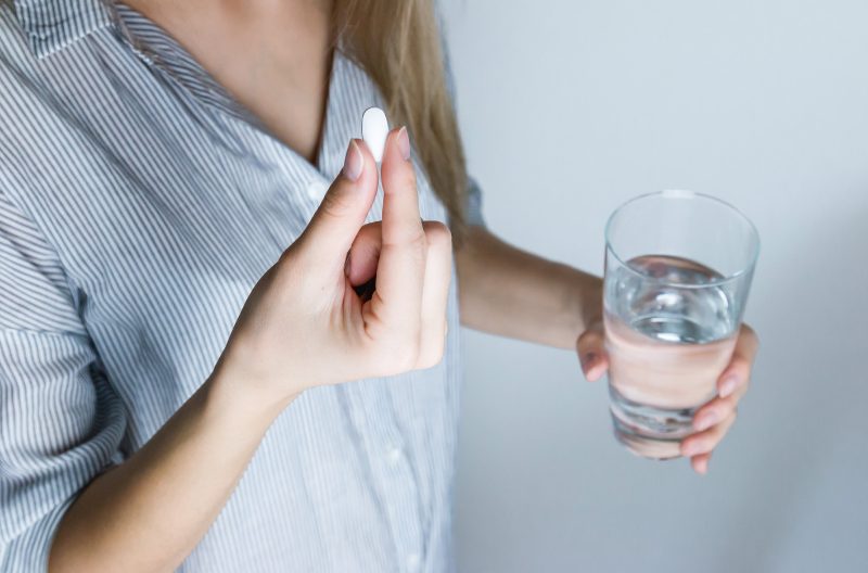 Woman holding onto a glass of water in one hand and a pill in the other