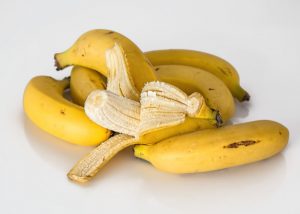 A peeled banana in a pile of whole bananas on a white table
