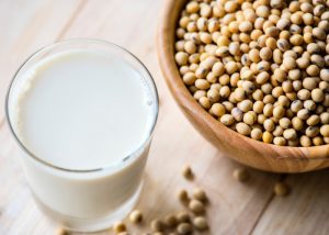 A glass of fortified soy milk next to a wooden bowl full of soy beans