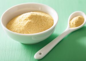 bowl and spoon full of nutritional yeast on a green table