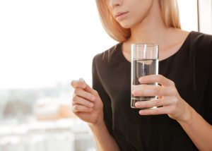 Woman holding a glass of water and a vitamin pill