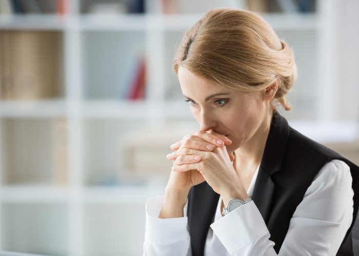 Middle-aged woman looking pensively ahead in concentration with her hands clasped