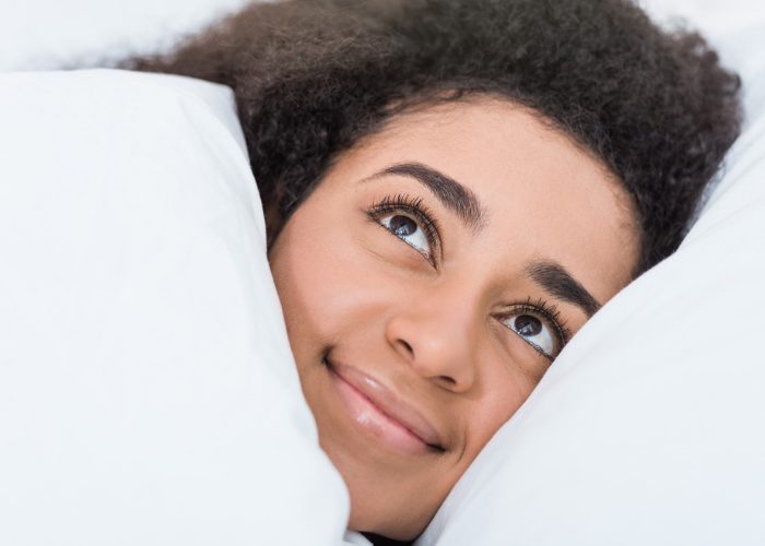 Woman smiling in bed looking comfortable with her weighted blanket pulled over her