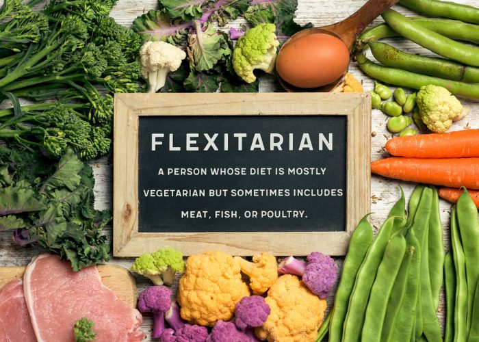 A blackboard with the definition of a flexitarian, surrounded mostly by fresh fruits and vegetables and only a small portion of chicken breast and eggs