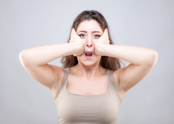 Woman doing face yoga exercises, stretching her face with her two hands and putting her lips inwards