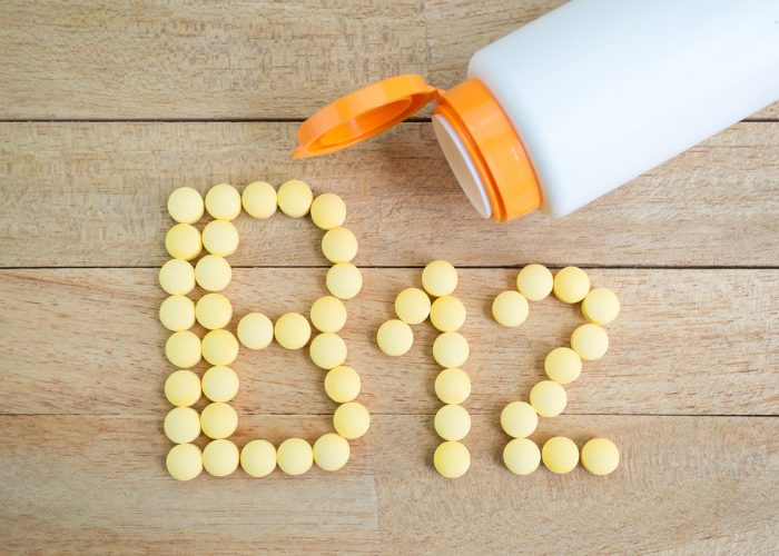 An open bottle next to yellow B12 pills spelling out "B12" on a table